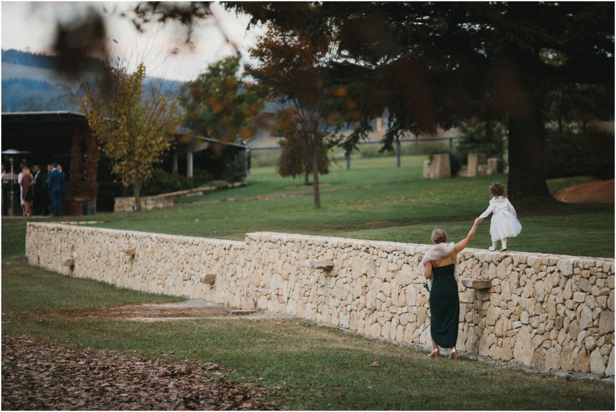A child walks hand in hand with her mother along a stone wall