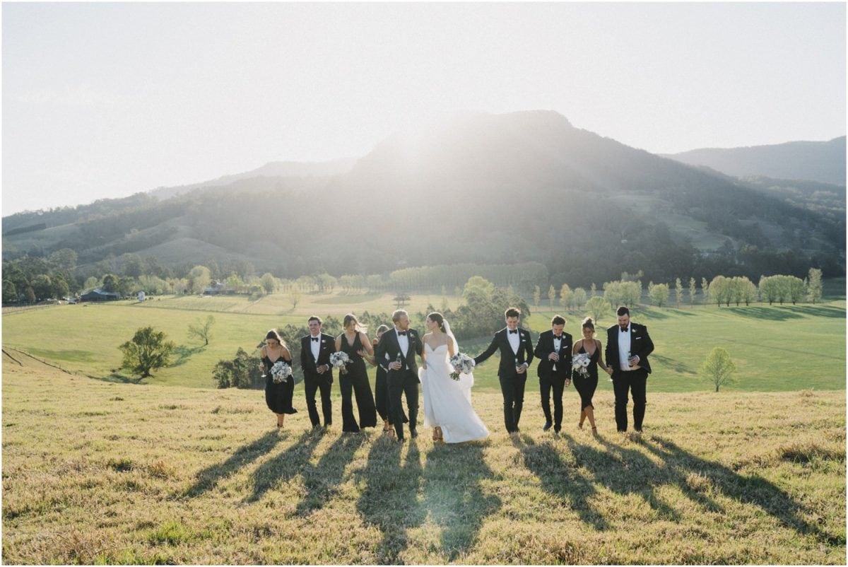 A bridal party walk in a field near sunset after a Melross wedding