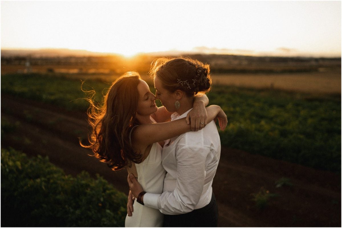 A newly married same sex couple in a potato field at sunset after their Quamby Home wedding