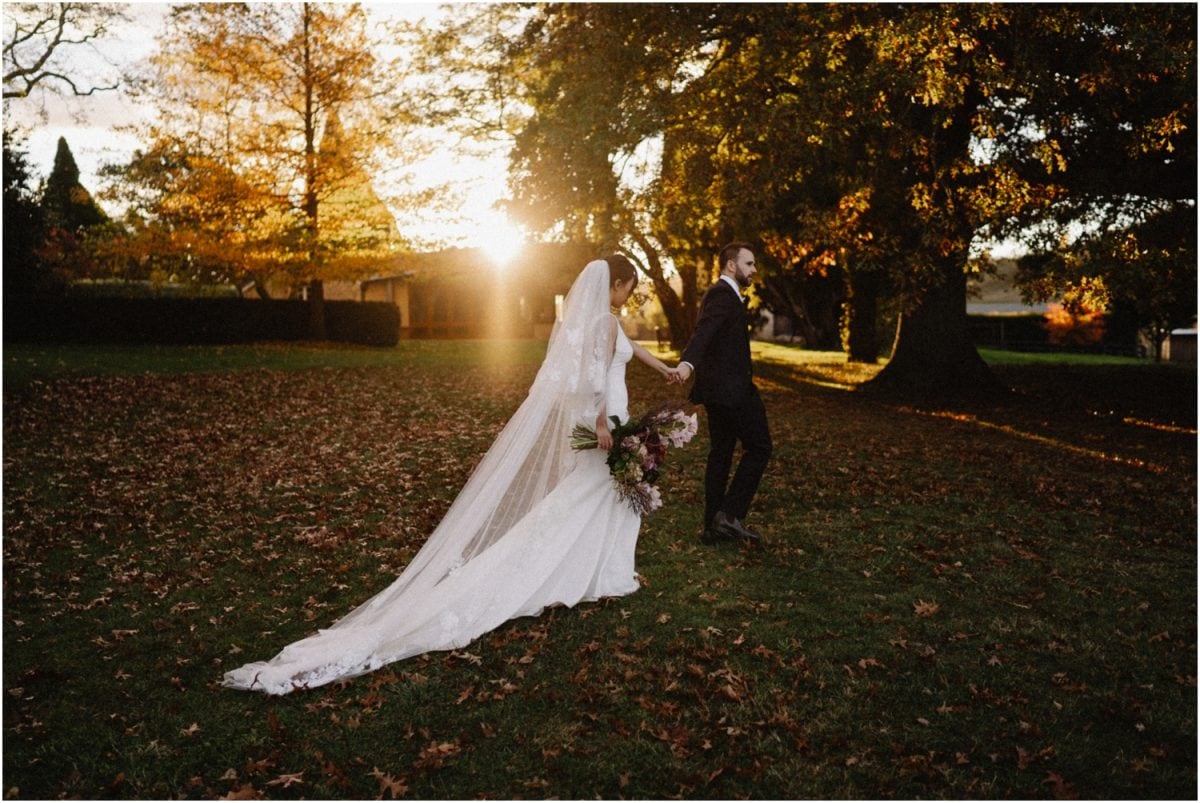 A newly married couple walk through fallen autumn leaves at sunset at their Bendooley Estate wedding