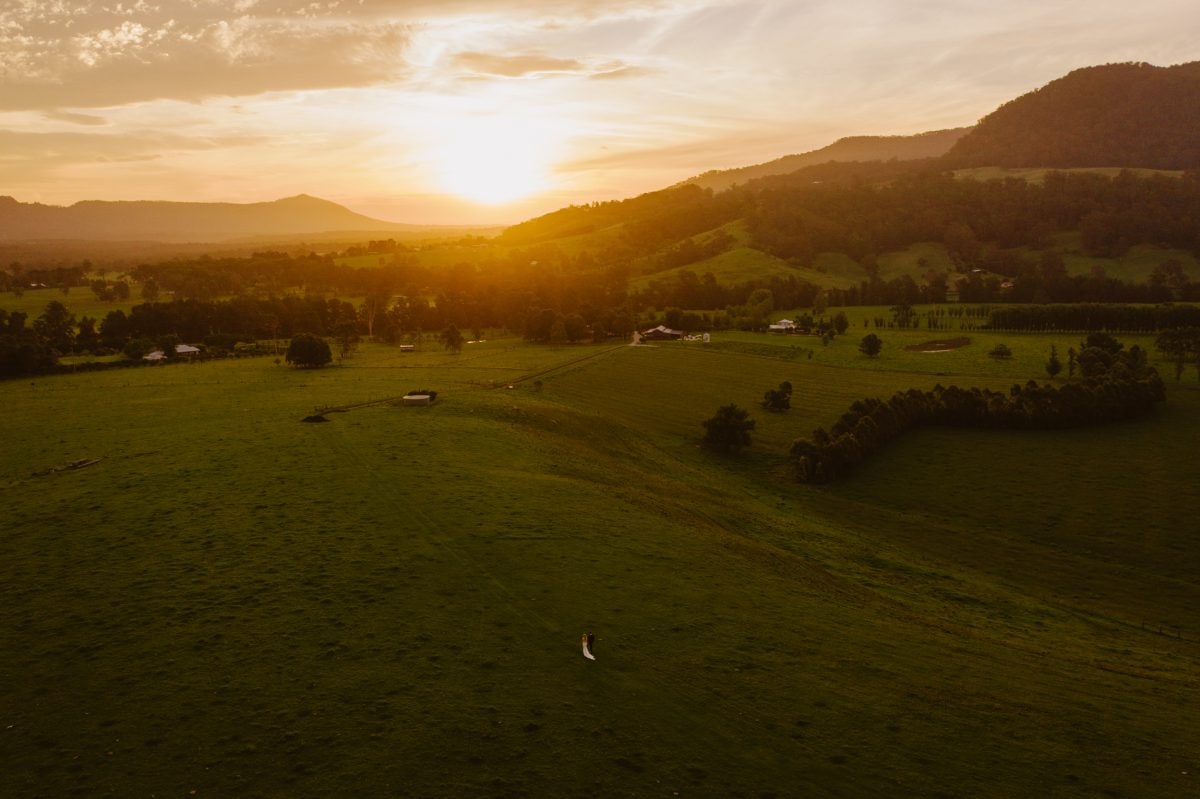 Drone photo of a bride and groom at sunset walking through a field. Photo by Southern Highlands Wedding Photographer Thomas Stewart.