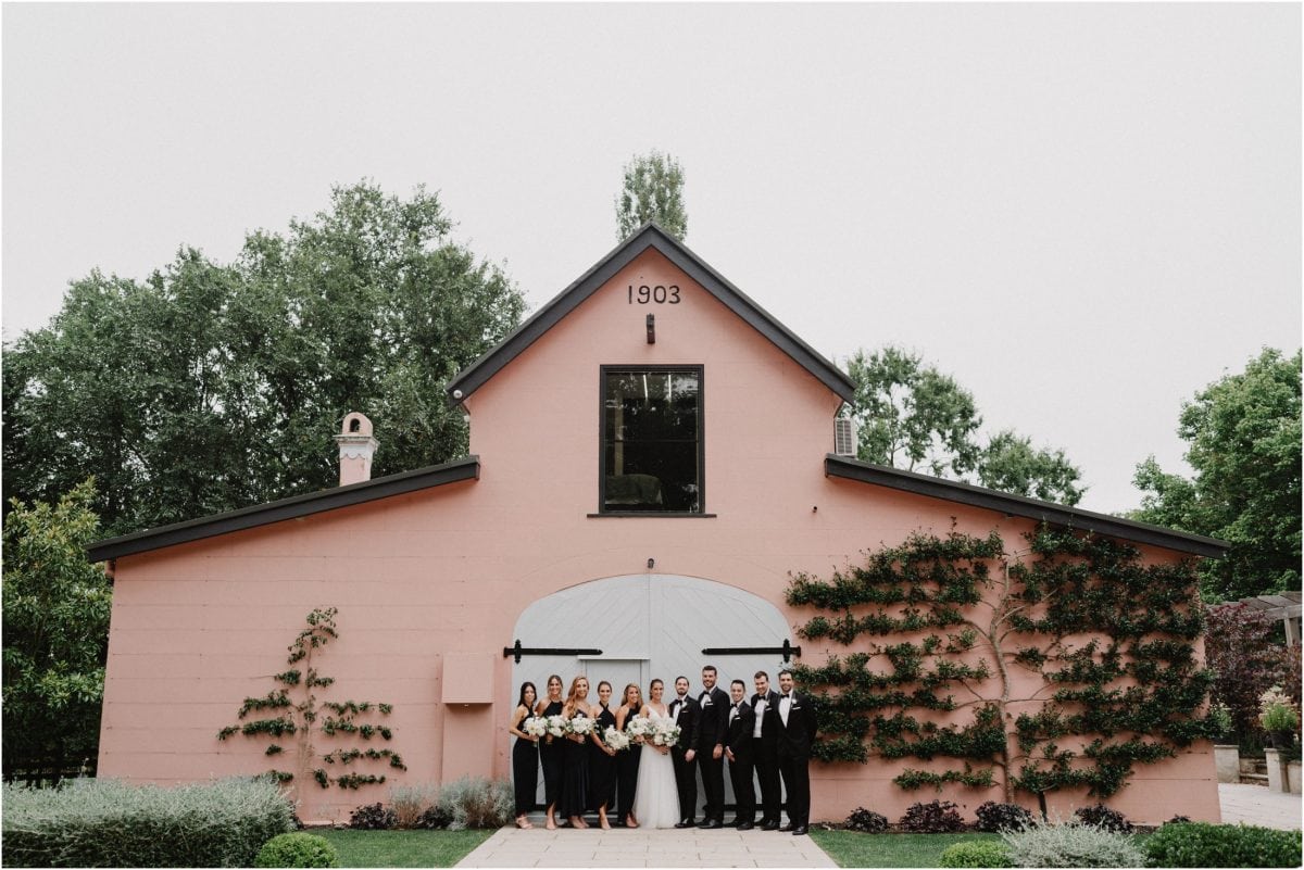 A bridal party pose for a photo in front of an old barn at a Mona Farm Wedding